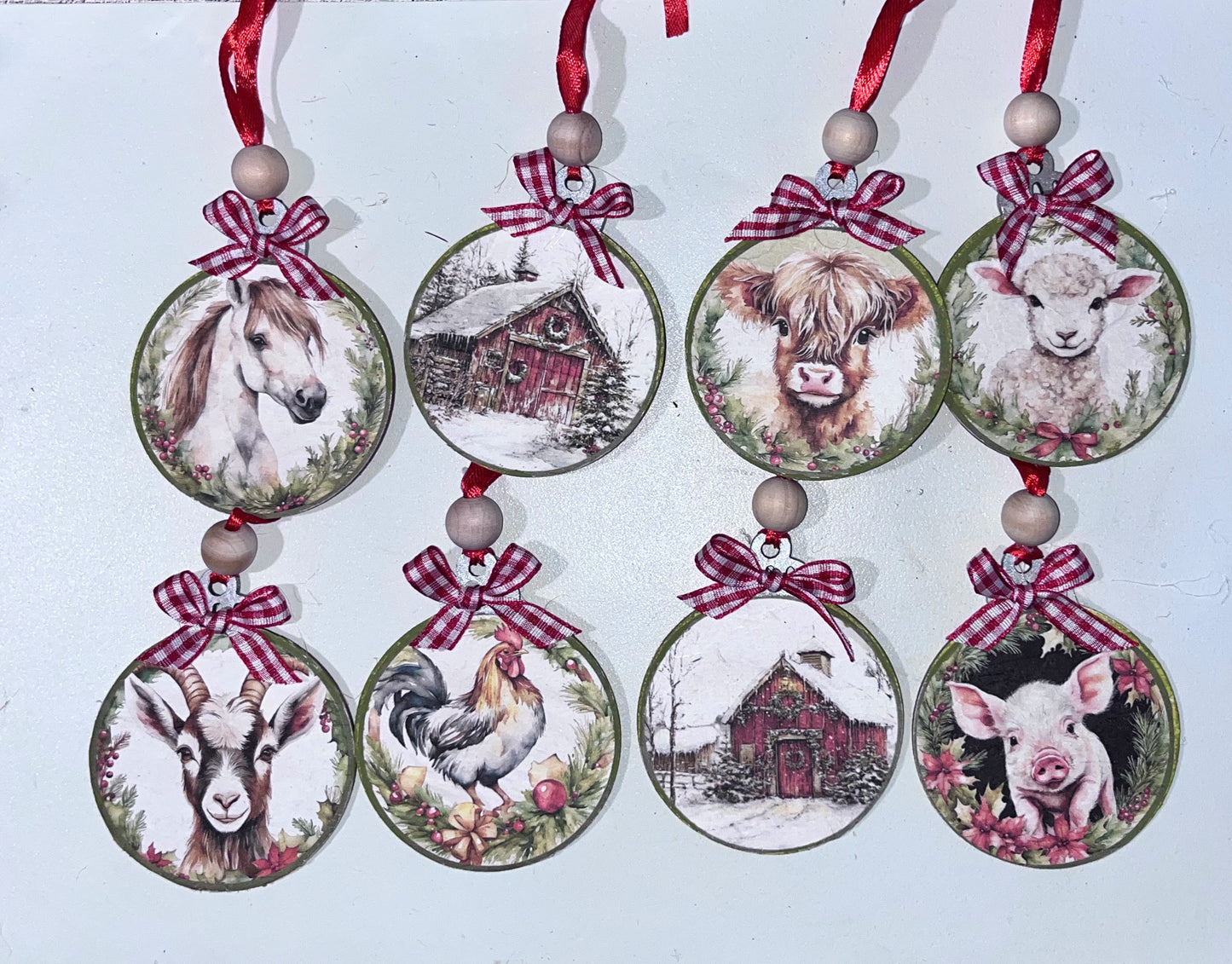 Set of eight farmhouse Christmas ornaments featuring a white horse, snowy red barn, highland cow, lamb, goat, rooster, winter barn, and piglet on 3-inch wooden rounds with red ribbon, gingham bows, and wood beads.