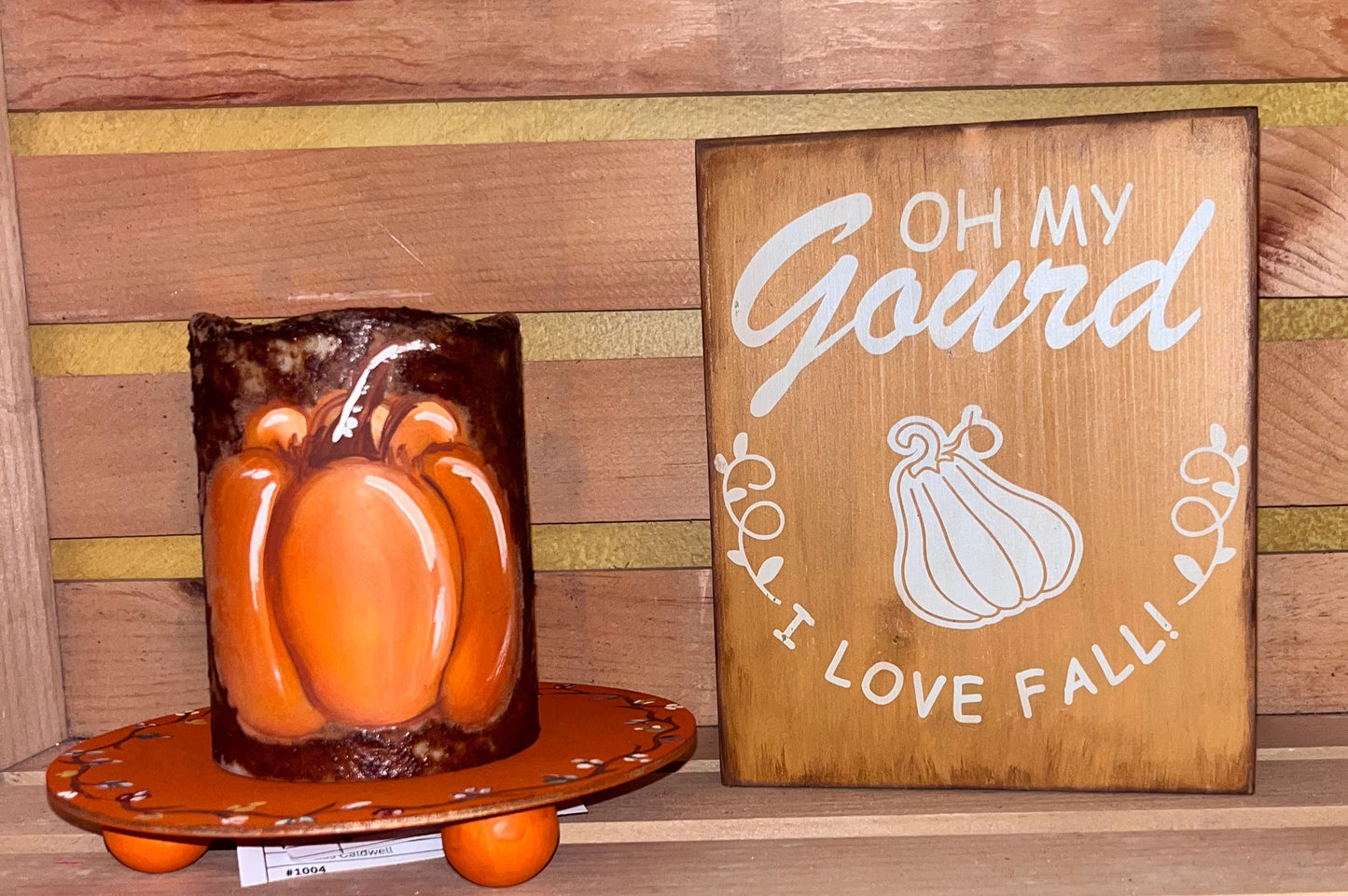 Hand-painted grungy flameless pumpkin candle displayed on a small orange pedestal next to a rustic wood sign that reads “Oh My Gourd, I Love Fall!” — set against a wooden backdrop for cozy fall decor.