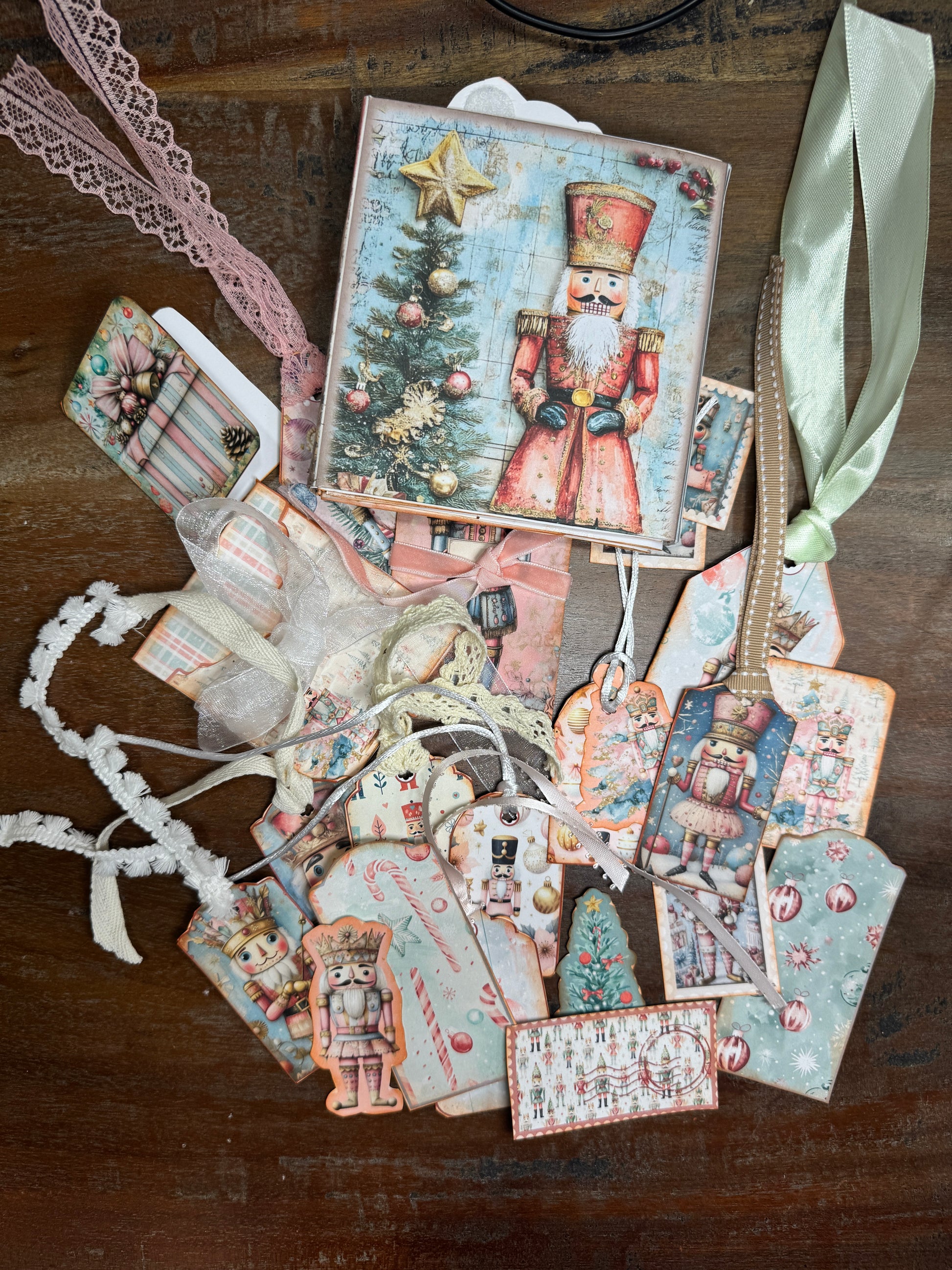 Handmade Nutcracker-themed junk journal folio displayed with an assortment of coordinating tags and inserts. The cover shows a red Nutcracker soldier beside a Christmas tree. Around it are various decorated tags featuring nutcrackers, ballerinas, candy canes, ornaments, and holiday patterns, each tied with ribbon or lace.