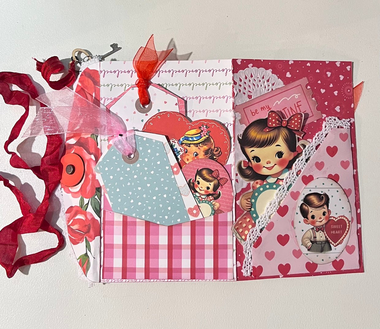 Back and cover pages of retro Valentine junk journal folio featuring tags, pockets, lace trim, ribbon closure, and vintage Valentine illustrations in pink and red tones