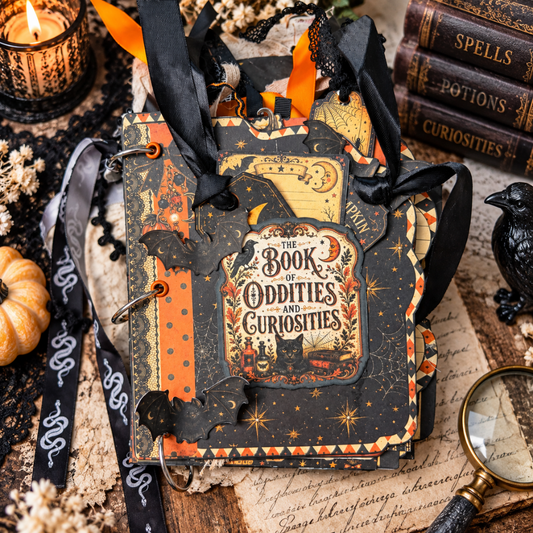 Front cover of the Book of Oddities and Curiosities Junk Journal decorated with bats, stars, spiderwebs, tags, orange and black patterns, and layered Halloween embellishments.