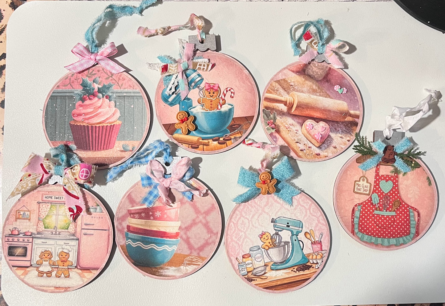 Set of eight pink Christmas Bake Shop ornaments featuring cupcakes, gingerbread cookies, stand mixers, rolling pin scene, retro kitchen, stacked bowls, and polka-dot apron, decorated with pastel ribbons, fabric ties, and gingerbread embellishments.
