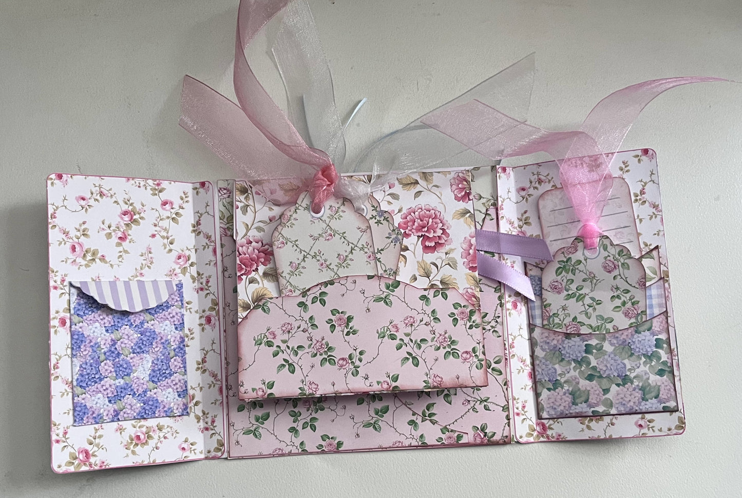 Close-up of Le’ Gated Garden folio cover artwork featuring vintage gate, pink blossoms, and watercolor landscape.