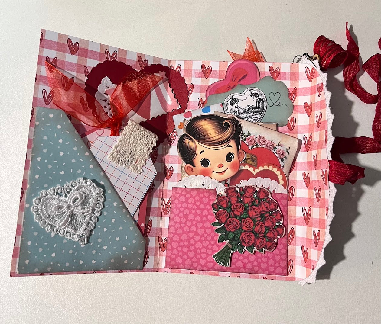 Inside view of retro Valentine junk journal folio with gingham heart background, layered pockets, vintage sweetheart graphics, lace details, and ribbon embellishments