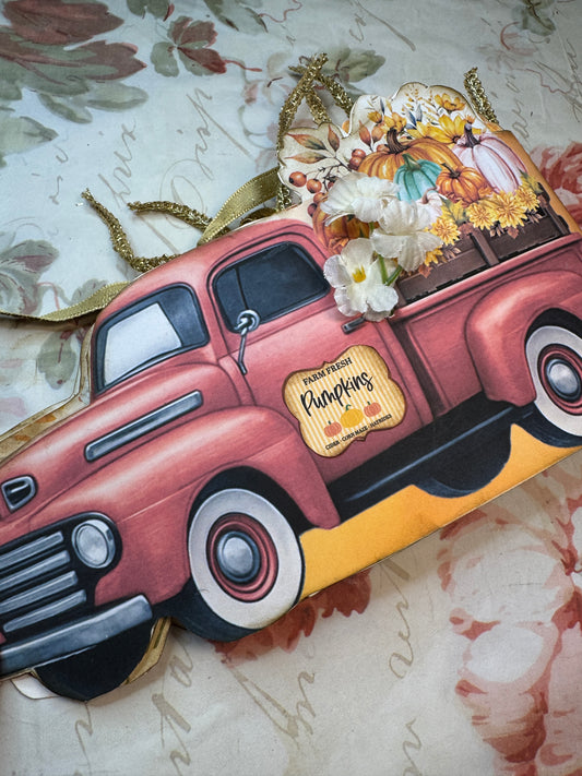 Fall-themed junk journal folio shaped like a vintage red pickup truck, filled with colorful pumpkins, sunflowers, and golden ribbon embellishments, resting on a floral background