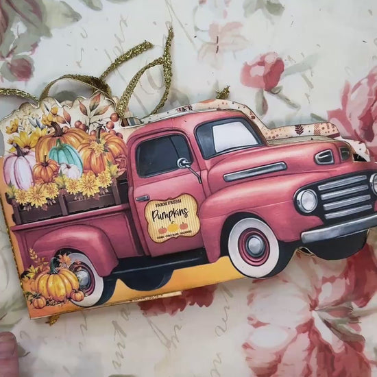 Fall-themed junk journal folio shaped like a vintage red pickup truck, filled with colorful pumpkins, sunflowers, and golden ribbon embellishments, resting on a floral background