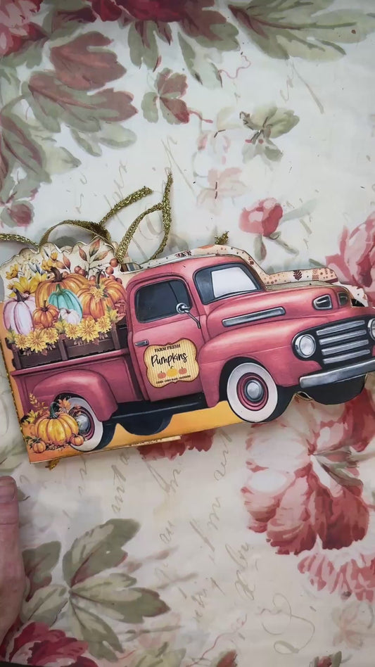 Fall-themed junk journal folio shaped like a vintage red pickup truck, filled with colorful pumpkins, sunflowers, and golden ribbon embellishments, resting on a floral background