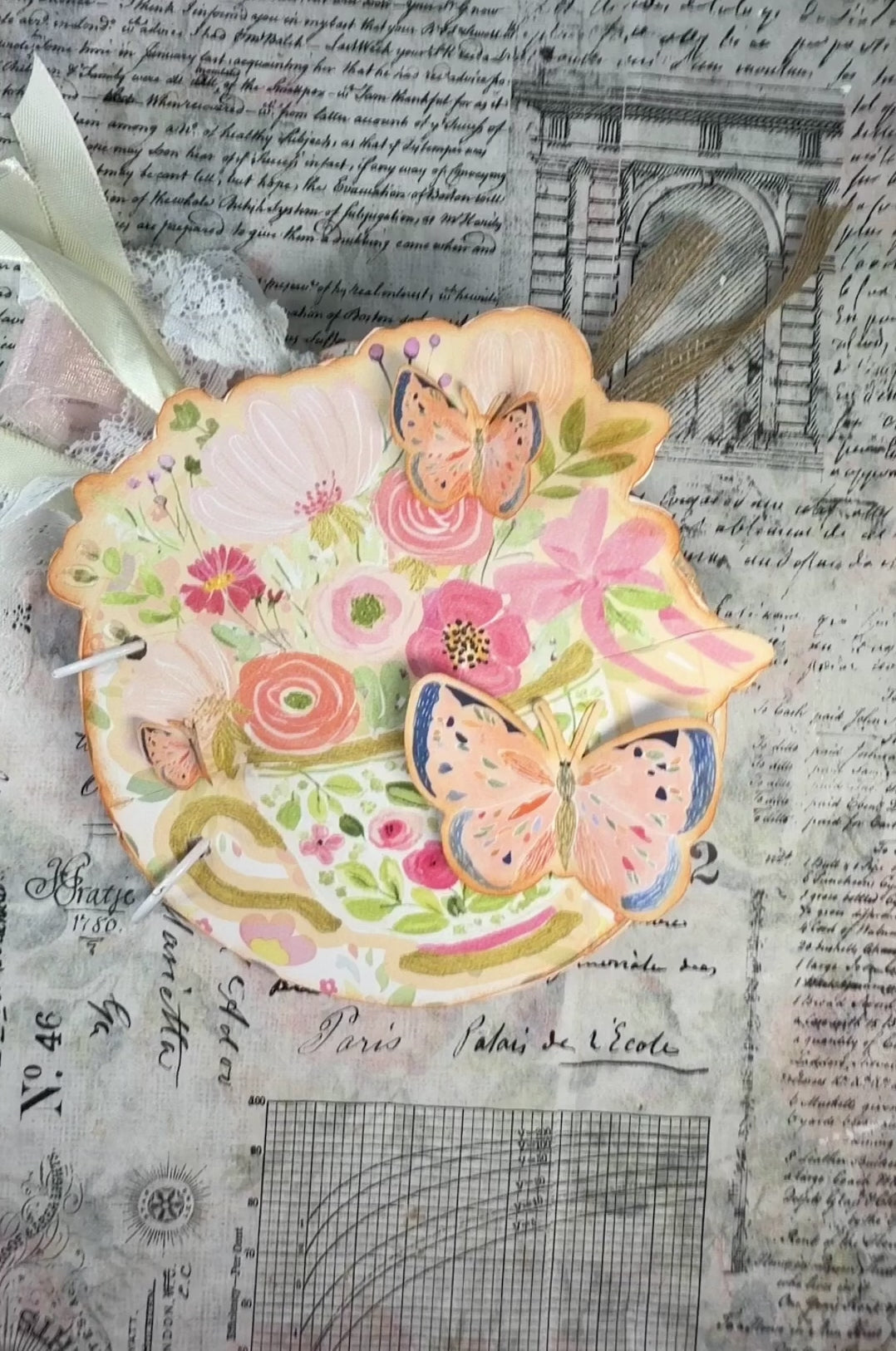 Hands flip through a floral teacup-shaped Afternoon Tea journal, revealing butterfly embellishments, pockets, tags, and ribbons.